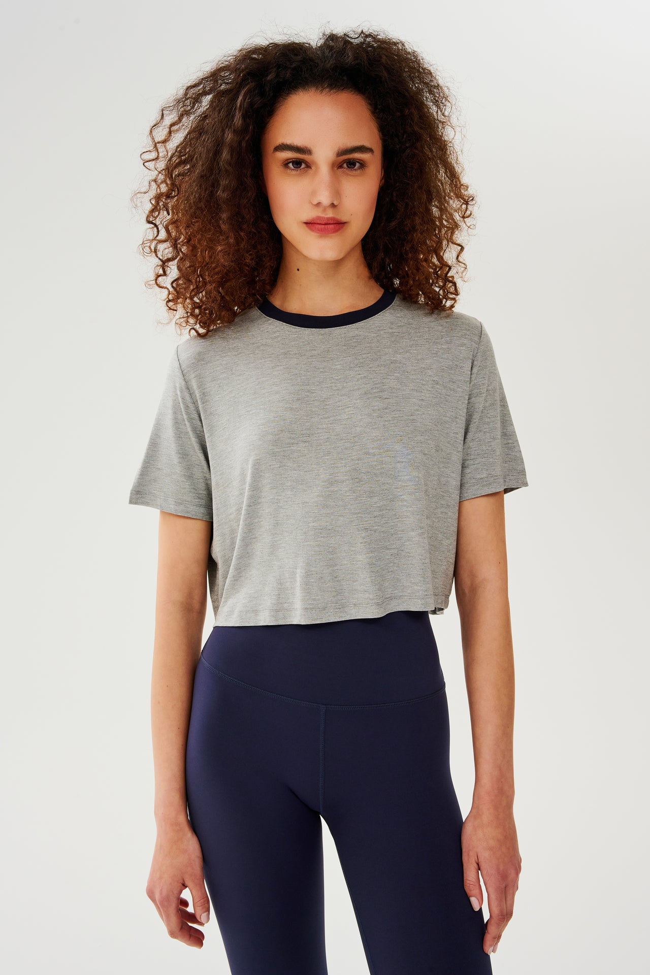 Front view of girl wearing  light grey cropped short sleeve t-shirt with thin dark blue neck hem and dark blue leggings 