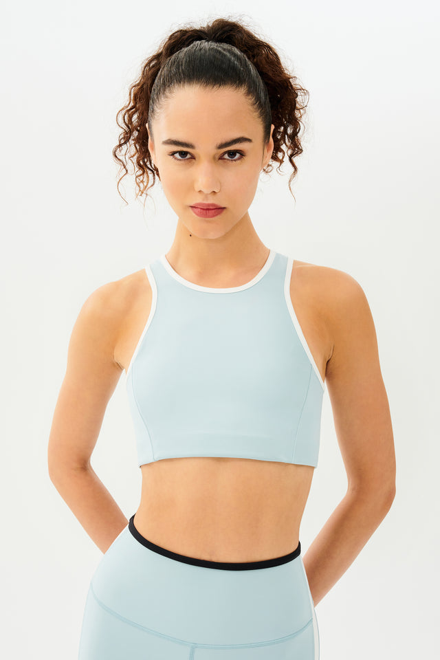 Front view of girl wearing light blue sports bra with white hem and light blue leggings with black stripe around the waistband and white stripe down the outer seam