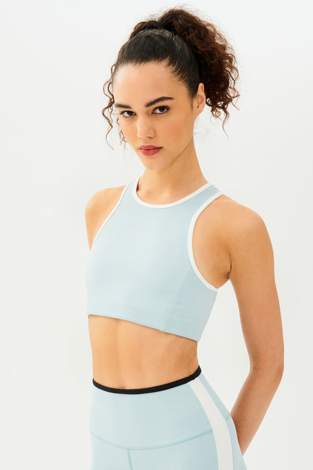 Side view of girl wearing light blue sports bra with white hem and light blue leggings with black stripe around the waistband and white stripe down the outer seam 