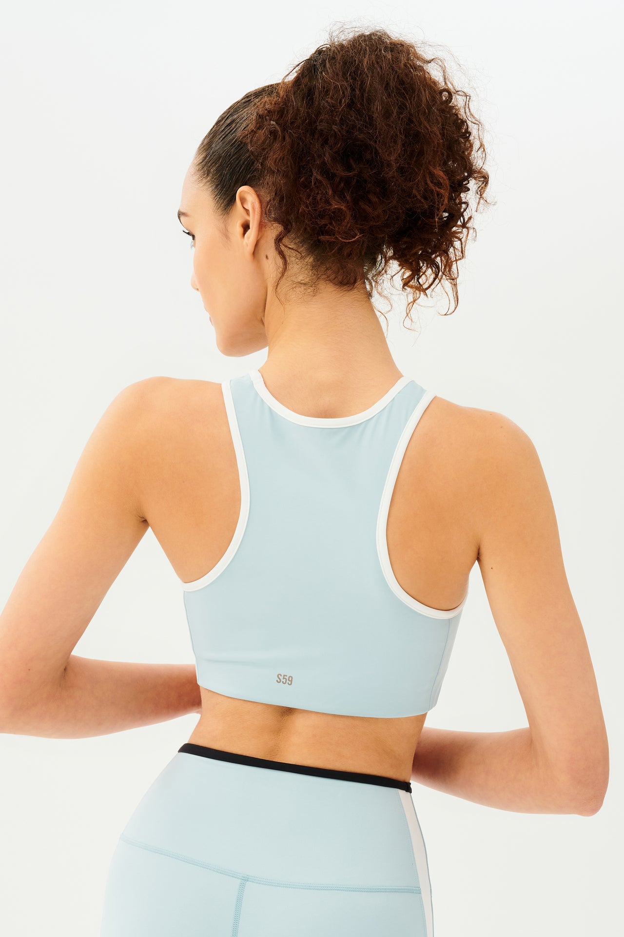 Back view of girl wearing light blue sports bra with white hem and light blue leggings with black stripe around the waistband and white stripe down the outer seam 