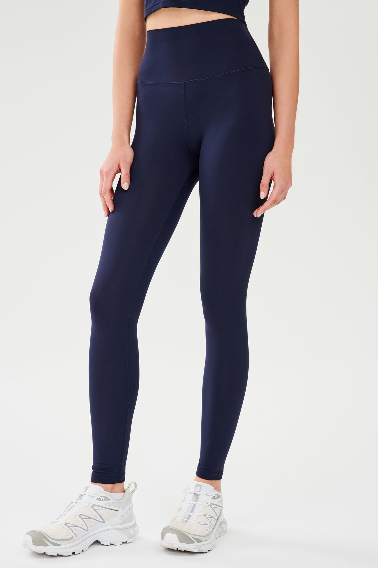 Front view of model wearing dark blue high waist leggings paired with white shoes