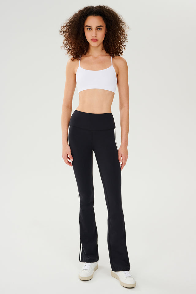 A woman wearing SPLITS59's Raquel High Waist Flared Legging in Black/White and a white top.