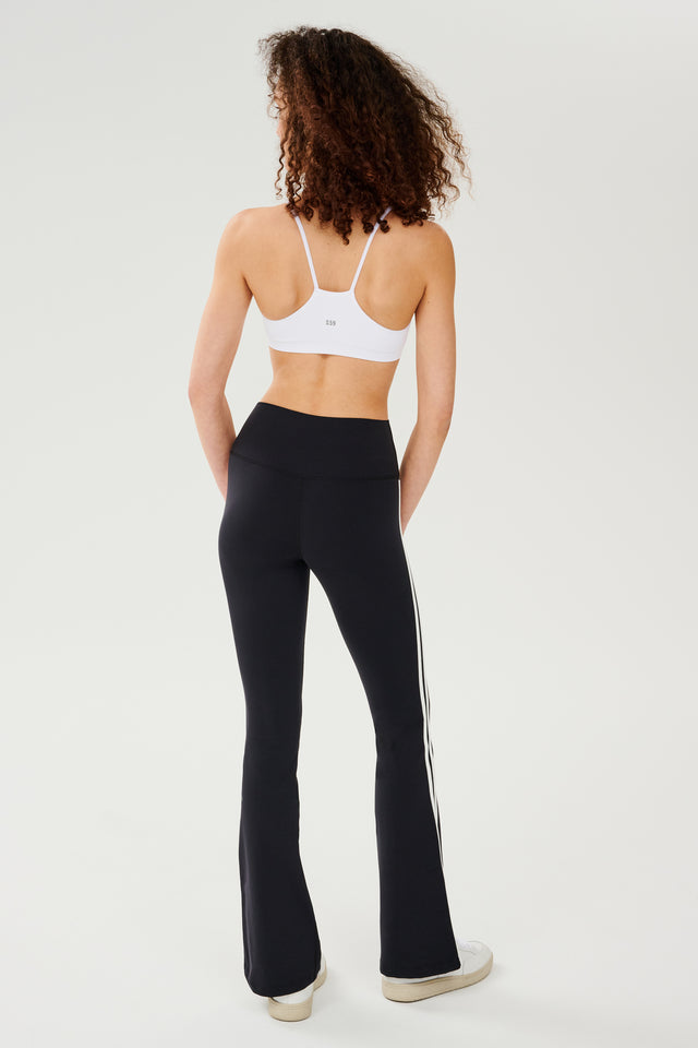 The back view of a woman wearing SPLITS59 Raquel High Waist Flared Legging in Black/White and a white top, perfect for gym workouts.