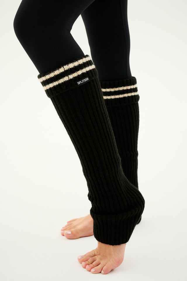 A person wearing the SPLITS59 Rib Beanie & Leg Warmer Set in Black/Creme, balanced barefoot on a light background, looks ready for cozy cashmere weather.