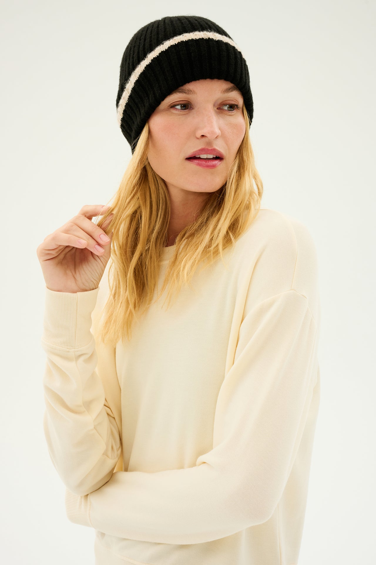 A person wearing a black and creme rib beanie from the SPLITS59 Rib Beanie & Leg Warmer Set and a light beige cashmere sweater, looking to the side.