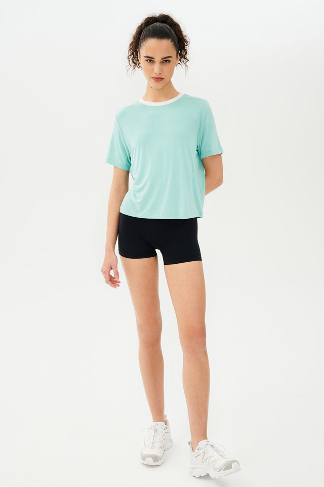 Full front view of girl wearing light blue cropped short sleeve t-shirt with thin white neck hem and black bike shorts with white shoes
