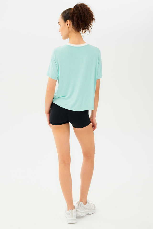 Full back view of girl wearing light blue cropped short sleeve t-shirt with thin white neck hem and black bike shorts with white shoes