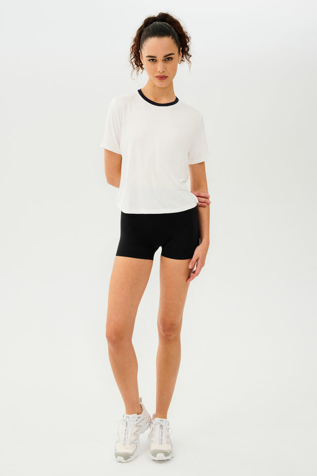 Full front view of girl wearing white cropped short sleeve t-shirt with thin black neck hem and black bike shorts with white shoes