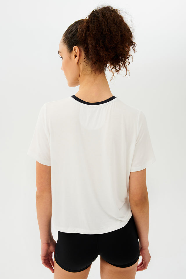Back view of girl wearing white cropped short sleeve t-shirt with thin black neck hem and black bike shorts 