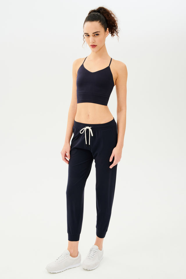 The model is wearing a Splits59 Loren Seamless Cami in Indigo with a shelf bra and joggers.