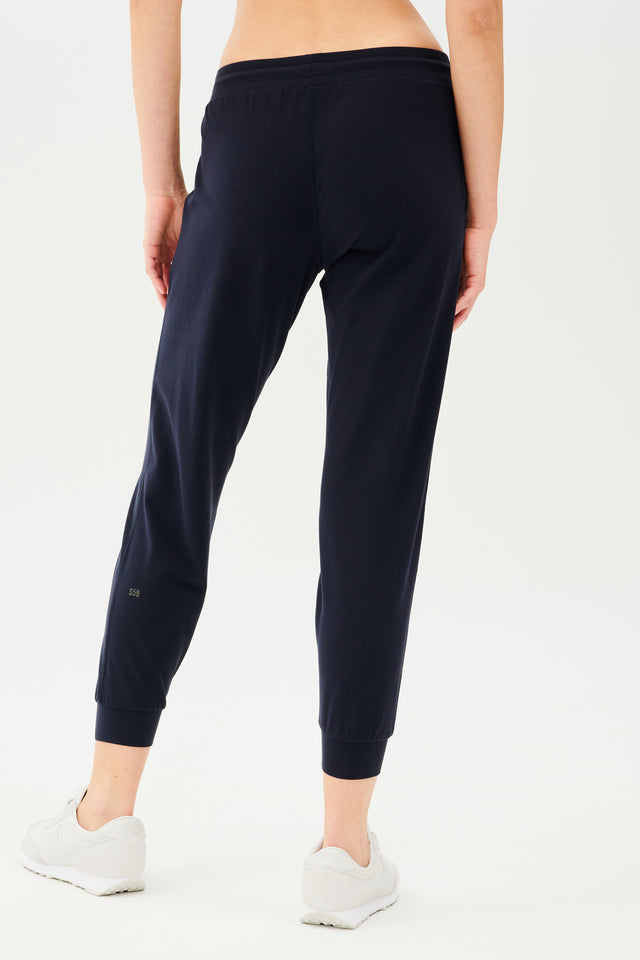 Back view of girl wearing dark blue sweatpants with black tie around waistband with white shoes 