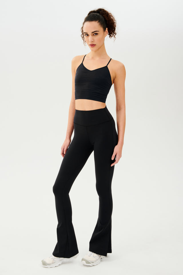A woman wearing SPLITS59 Raquel High Waist Flare w/ Split Hem in Black and a black crop top, both designed for gym workouts with 4-way stretch supplex fabric.