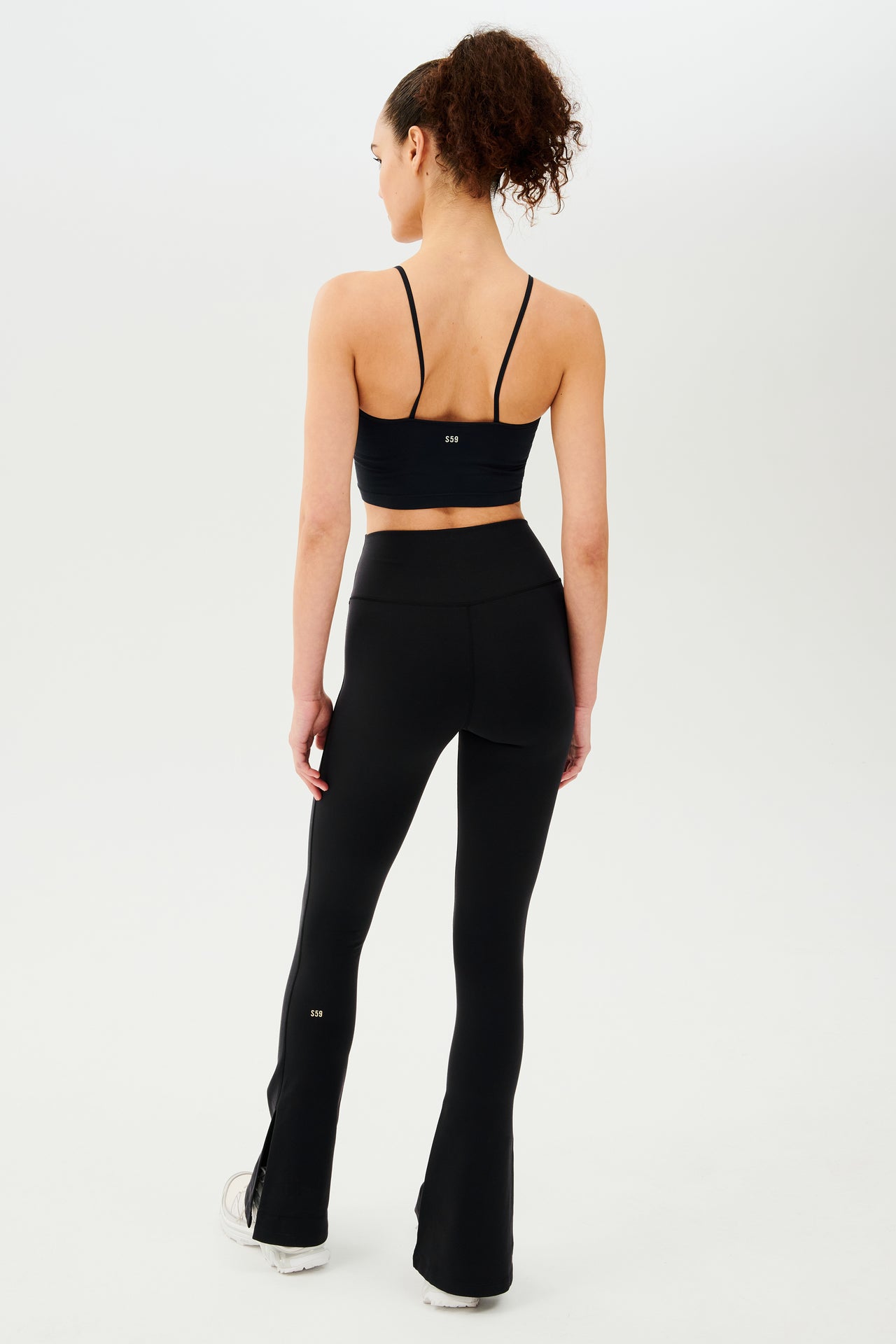 The back view of a woman in SPLITS59 Raquel High Waist Flare w/ Split Hem - Black leggings, perfect for gym workouts.