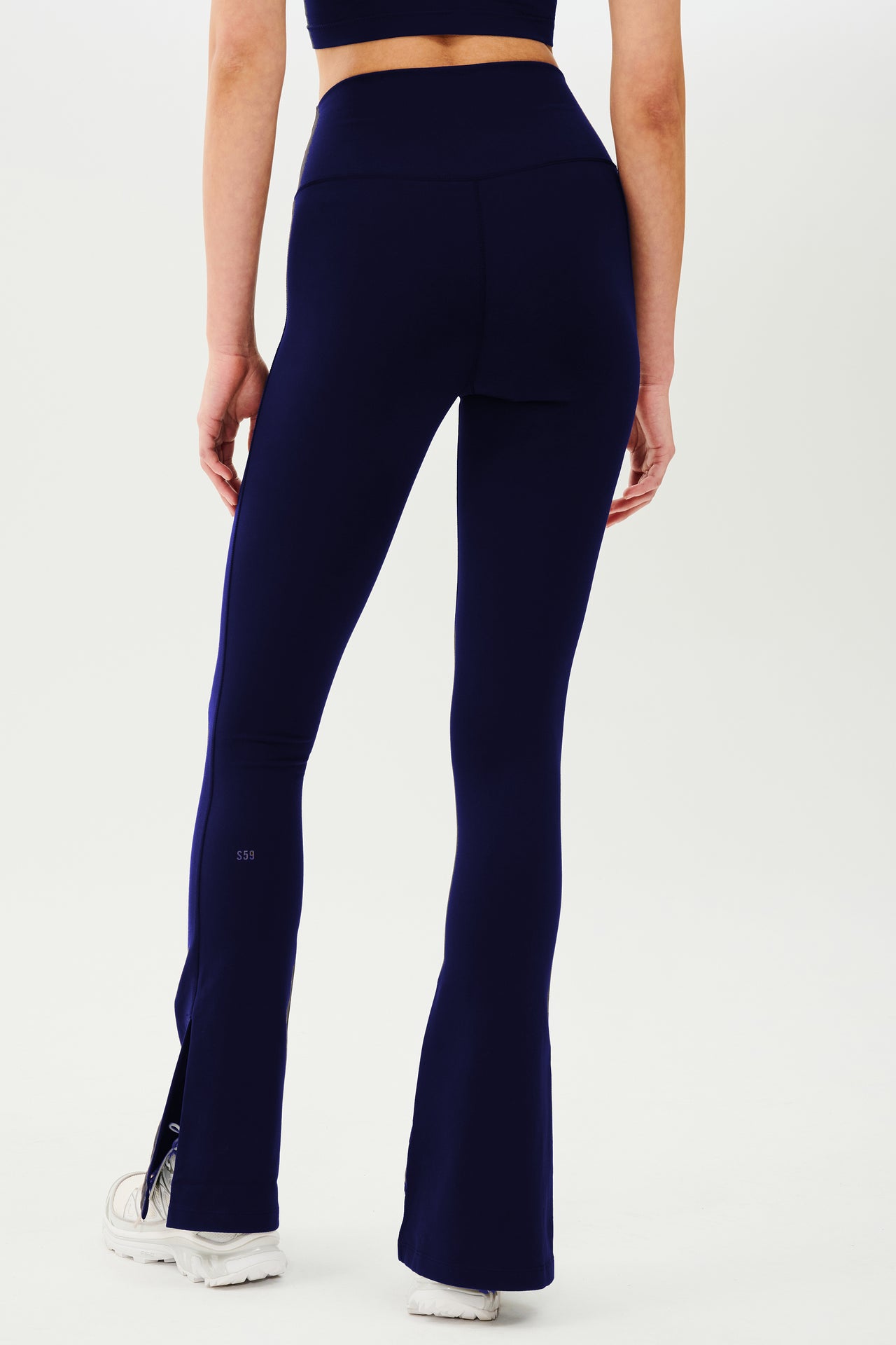 The back view of a woman wearing SPLITS59 Raquel High Waist Flare w/ Split Hem - Indigo leggings designed for workouts with 4-way stretch capability.