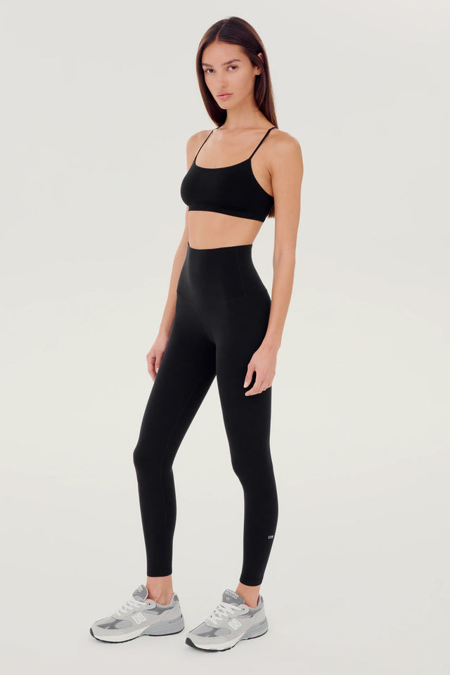 Full side view of girl wearing black leggings right above the ankle with black sports bra and grey shoes