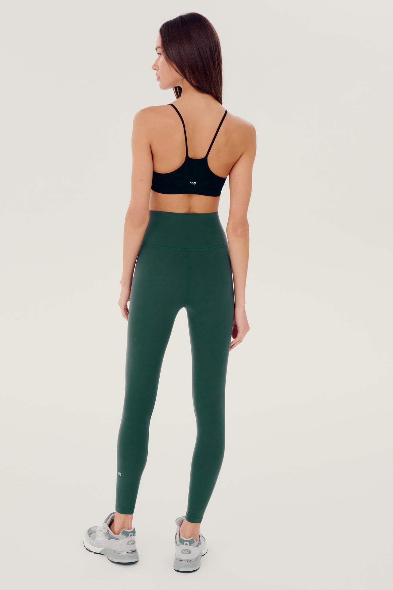 Full back view of girl wearing dark green leggings right above the ankle with black sports bra and grey shoes