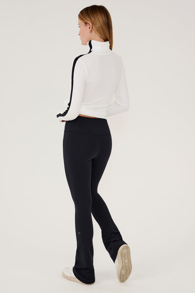 The back view of a woman wearing black leggings and a white SPLITS59 Jackson Rib Full Length Turtleneck - White/Black.