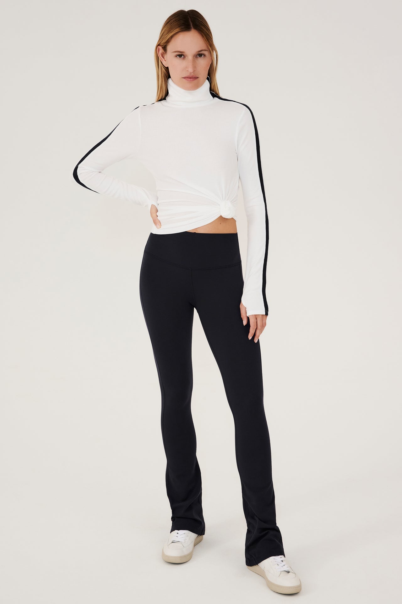A woman wearing black leggings and a SPLITS59 Jackson Rib Full Length Turtleneck - White/Black top.