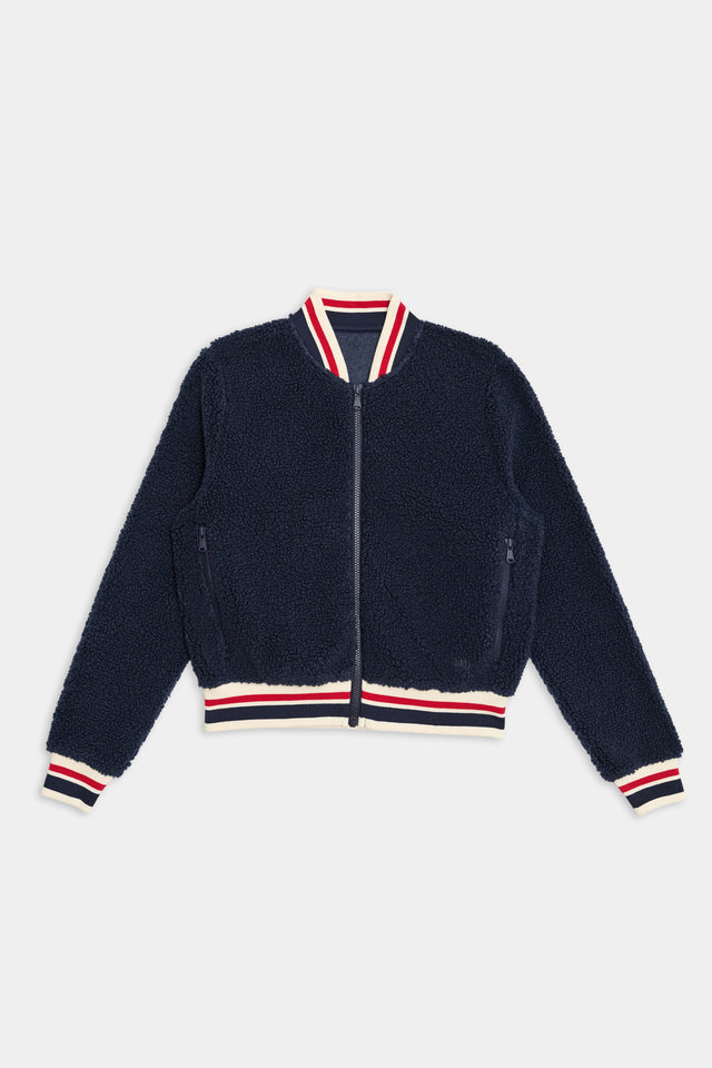 A 100% polyester navy blue fleece jacket with a front zipper, featuring red, white, and blue striped cuffs, collar, and hem. The product is called the Willa Sherpa Jacket - Indigo by SPLITS59.