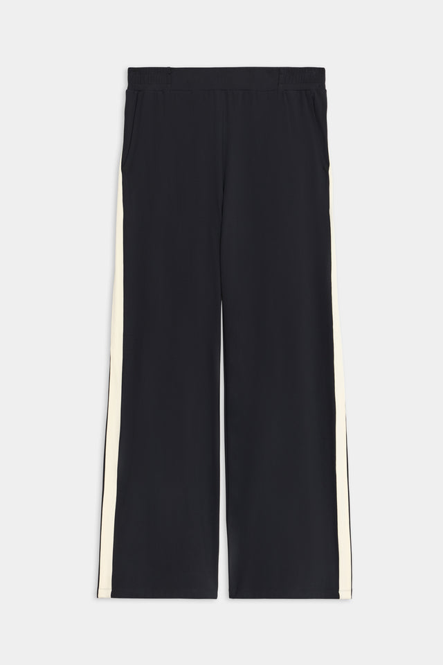 Introducing the SPLITS59 Luca Airweight Trouser with Stripe in Black/White: track pants featuring sleek white side stripes, ideal for casual outings. Made from ultra-luxurious Airweight fabric, these trousers provide exceptional comfort and style against a plain background.