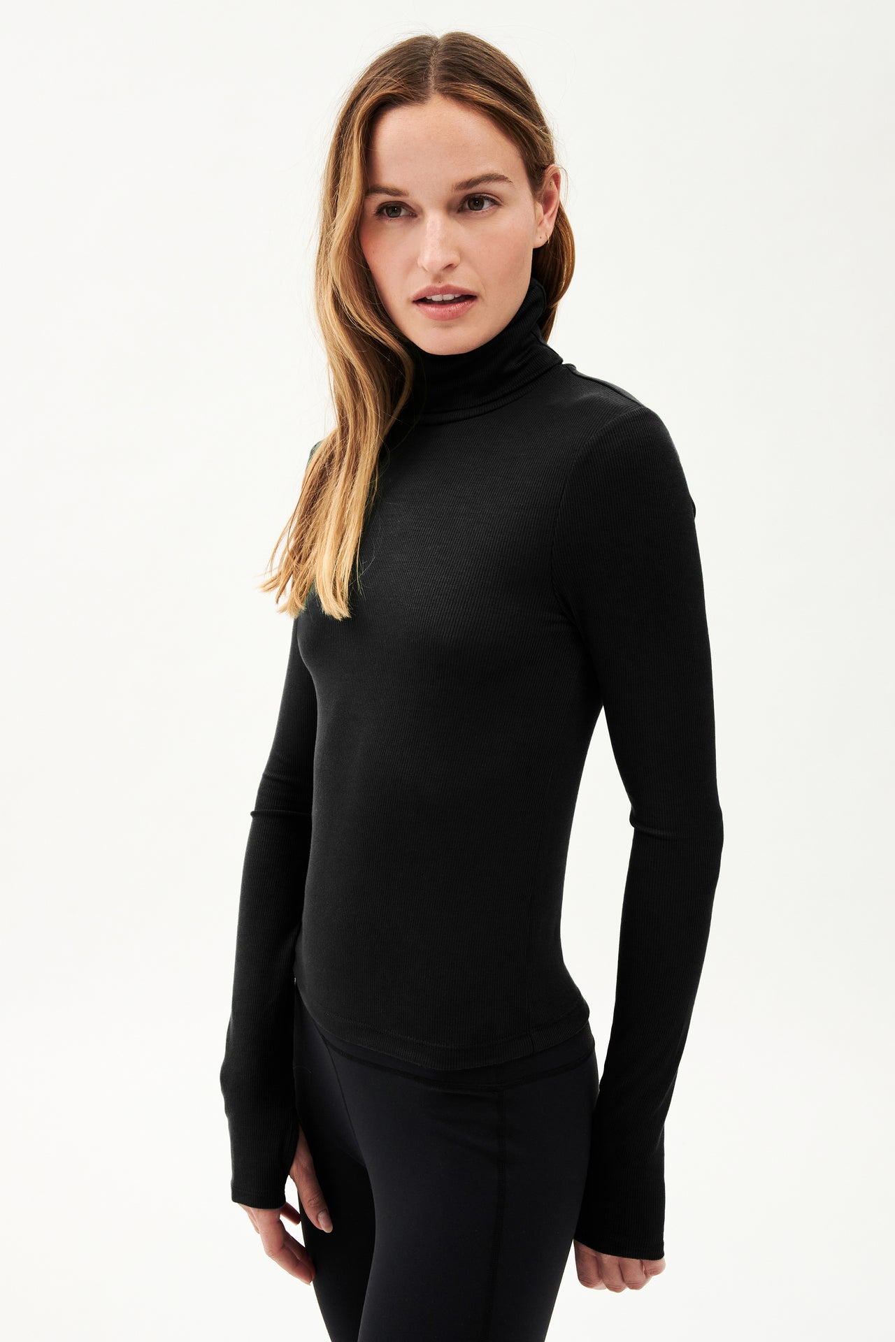 A woman wearing a SPLITS59 Jackson Rib Full Length Turtleneck in Black and leggings, ready for yoga.