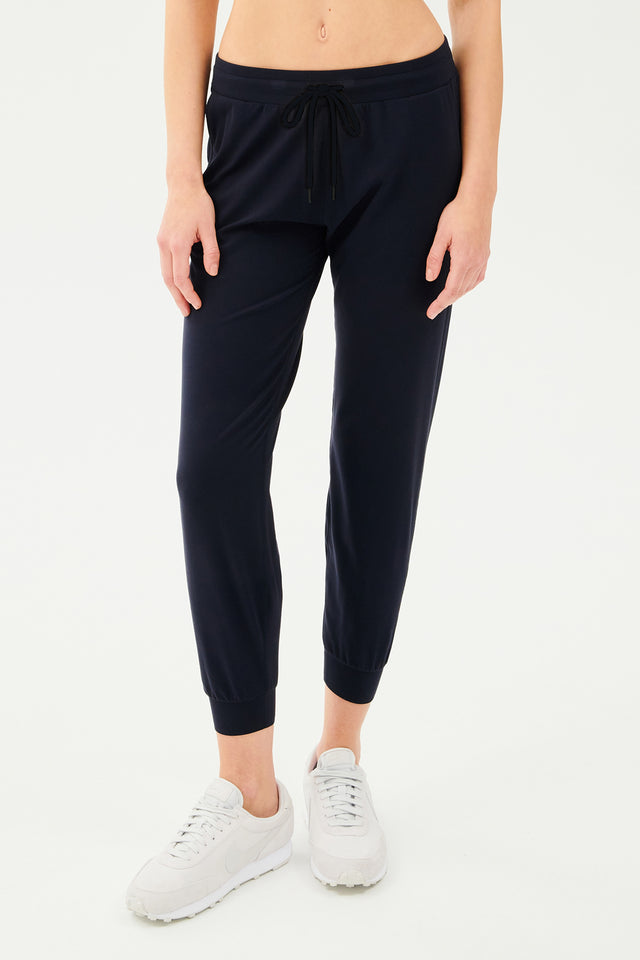 Front view of girl wearing dark blue sweatpants with black tie around waistband with white shoes 