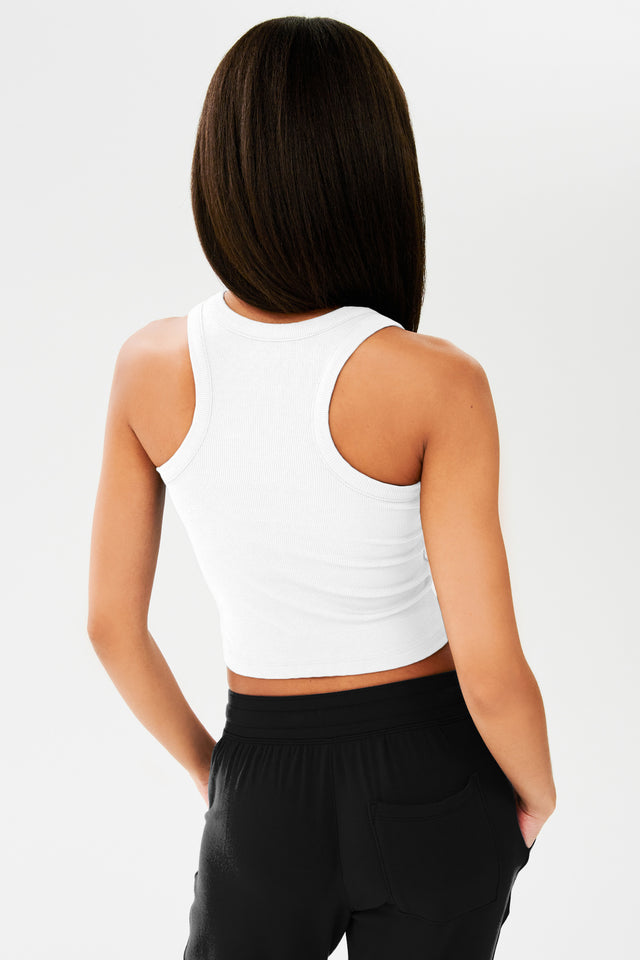 The back view of a woman wearing a white SPLITS59 Kiki Rib Crop Tank and black sweatpants.