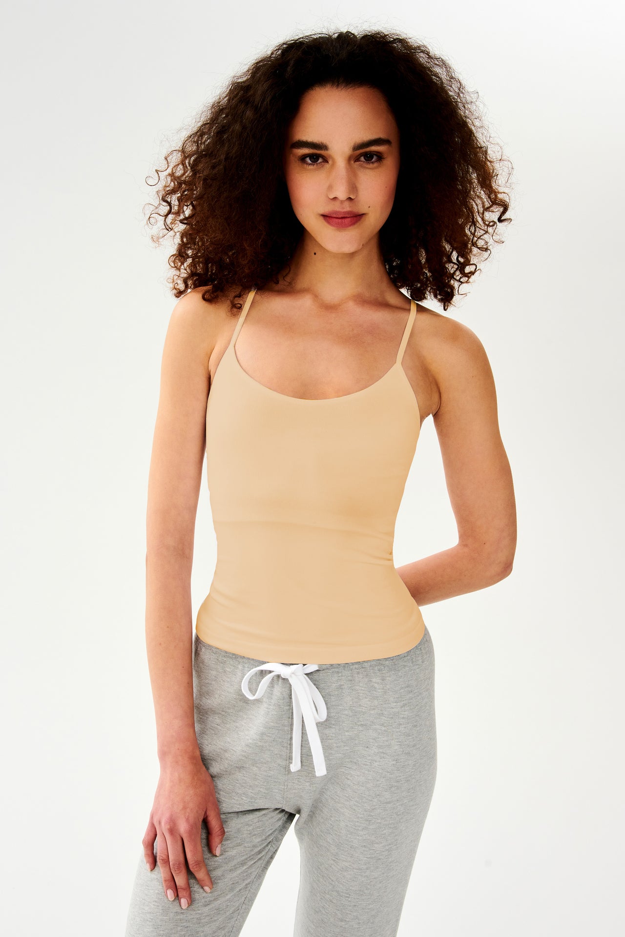 A woman in a SPLITS59 Loren Seamless Waist Length Tank - Nude with a built-in shelf bra and gray sweatpants.