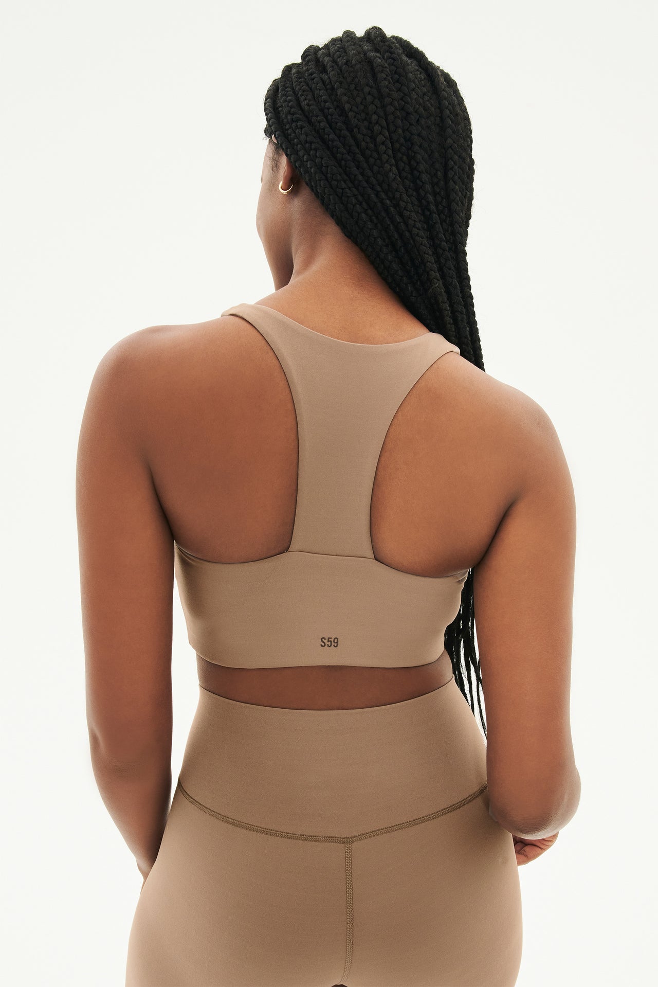 Back view of woman with black braids wearing light brown leggings  and light brown bra with racerback