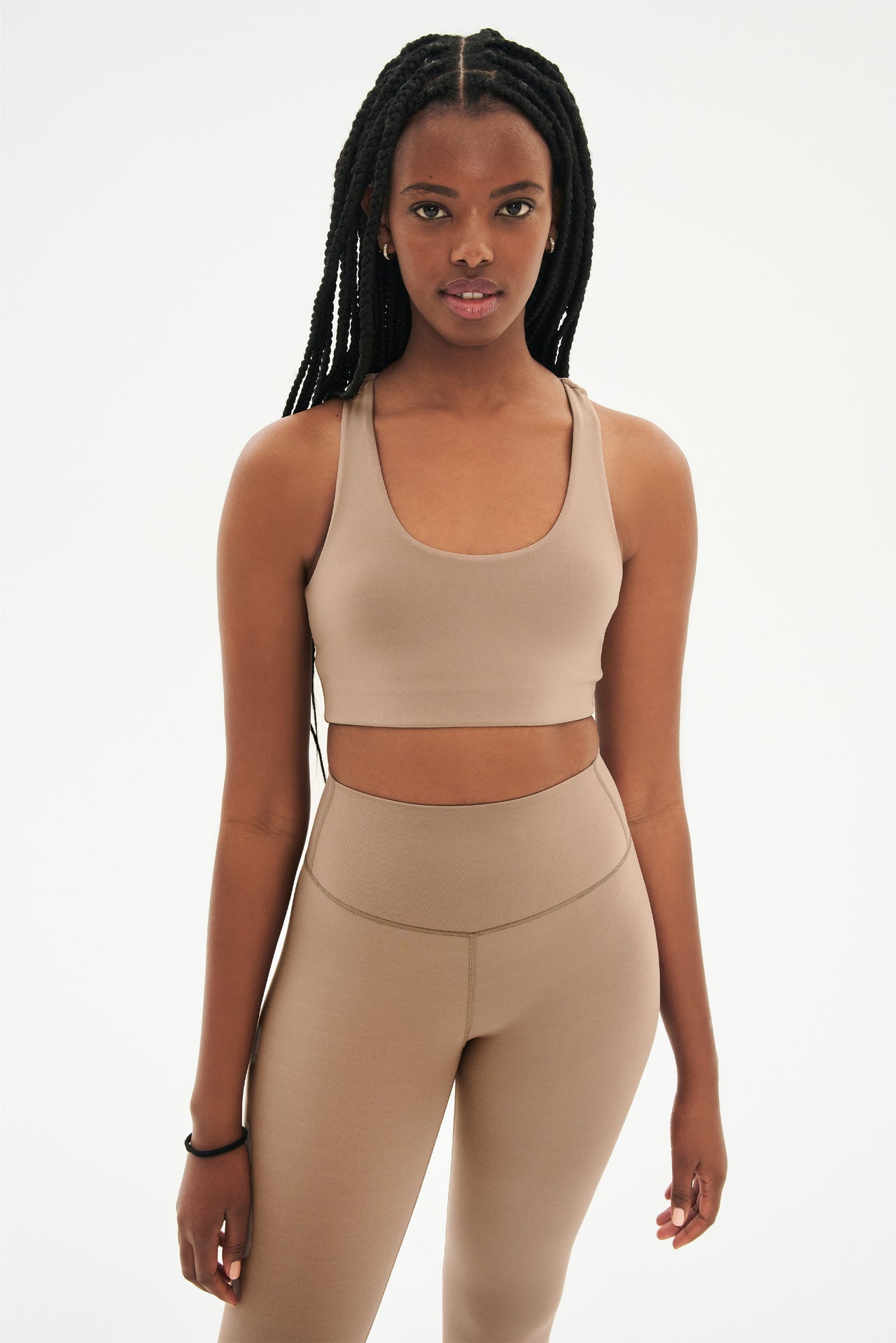 Front view of woman with black braids wearing light brown leggings and light brown bra