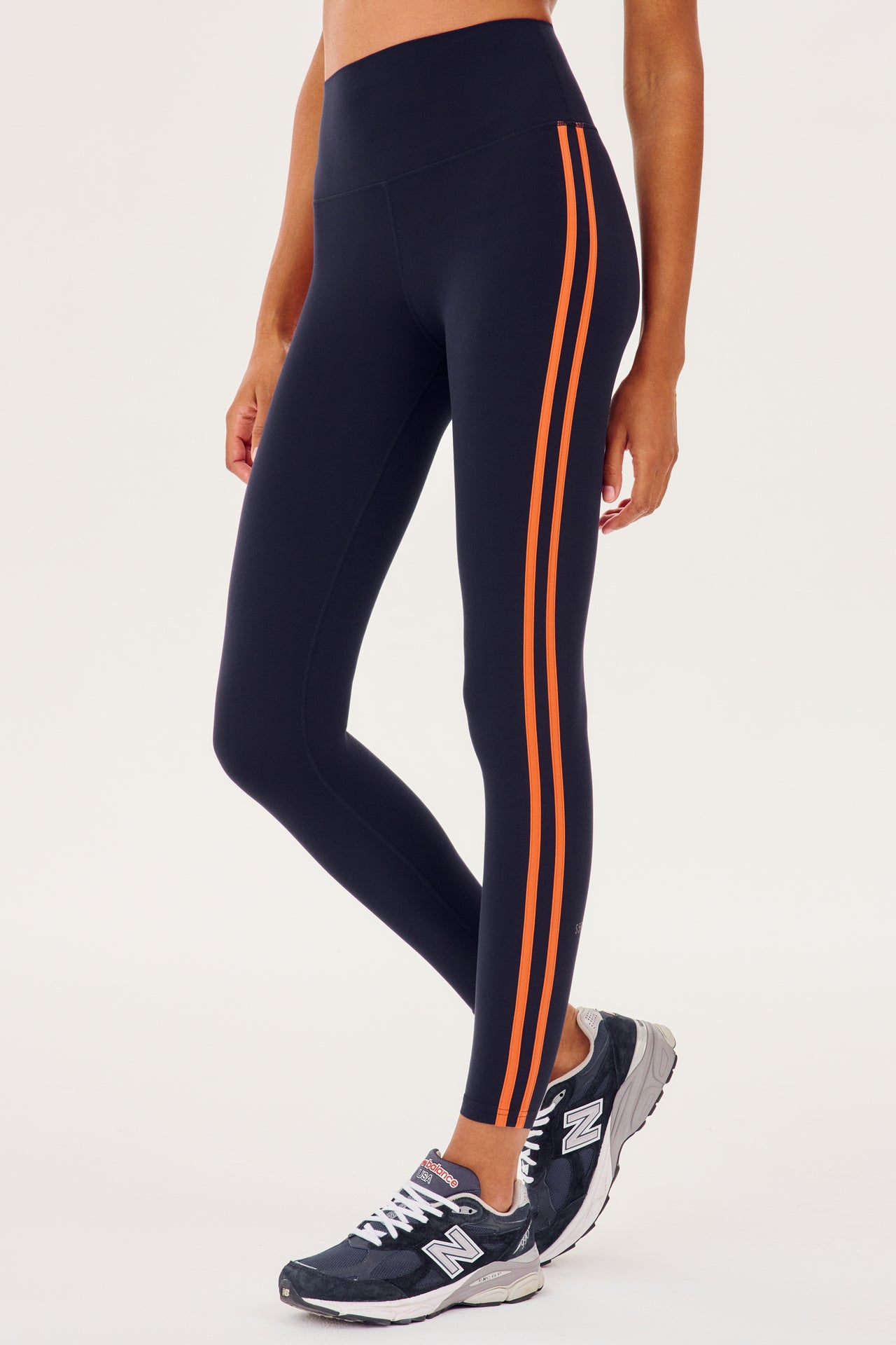 Side view of girl wearing dark blue leggings with two thin red stripes down the side with dark blue shoes