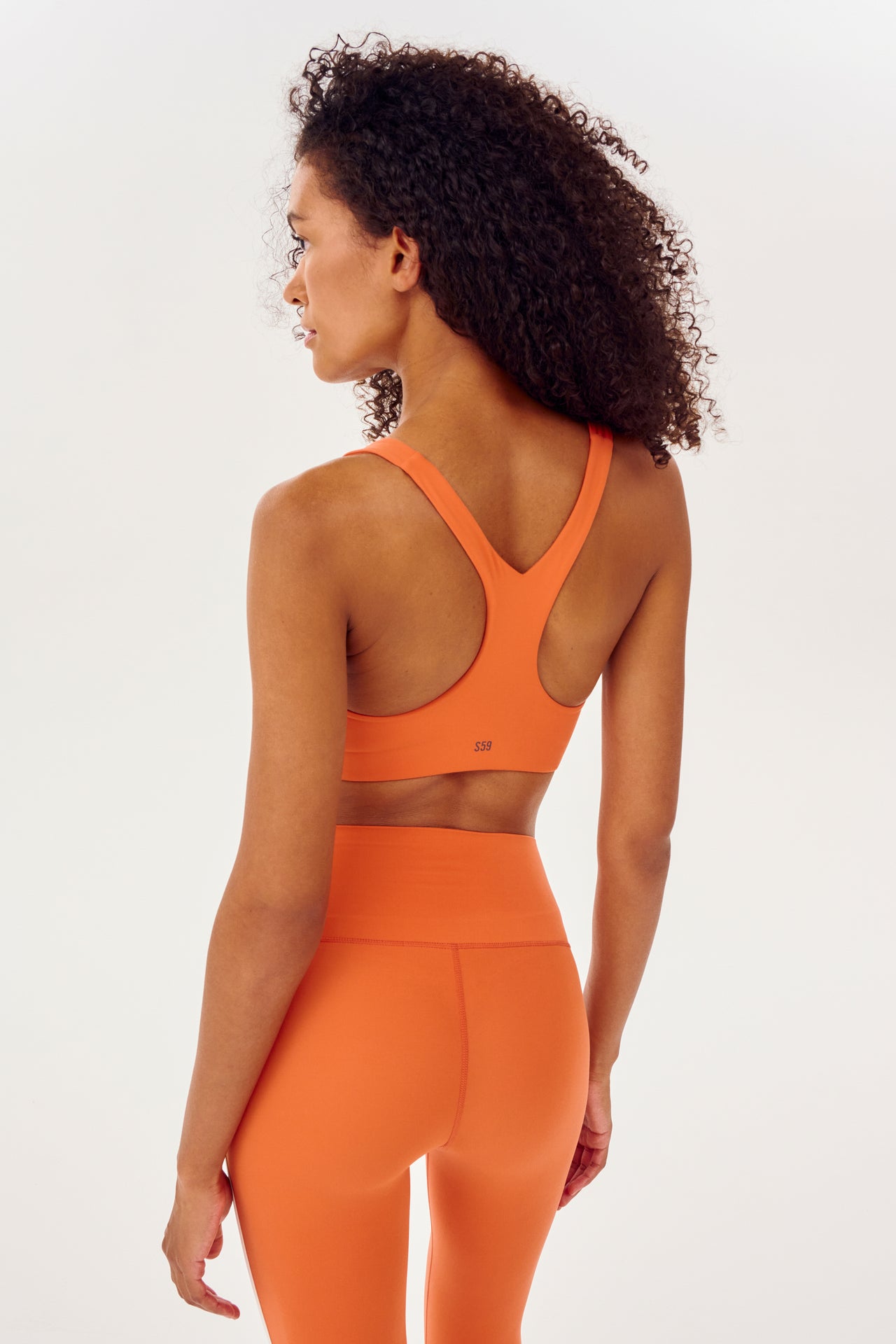 Back view of girl wearing orange sports bra with two thin white stripes  down the side and orange leggings 