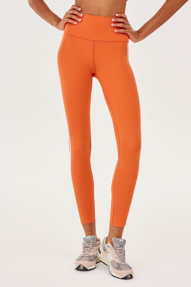 Front view of girl wearing orange leggings with two thin white stripes down the side with white shoes