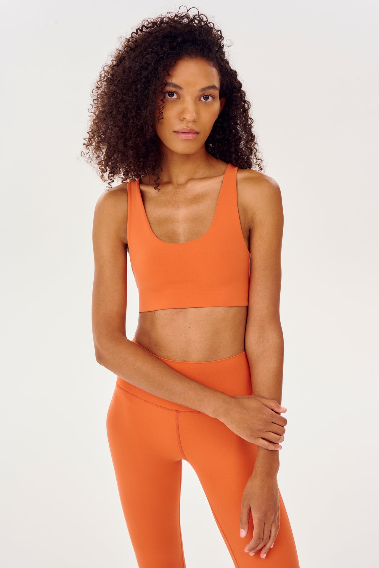 Front view of girl wearing orange sports bra with two thin white stripes  down the side and orange leggings 