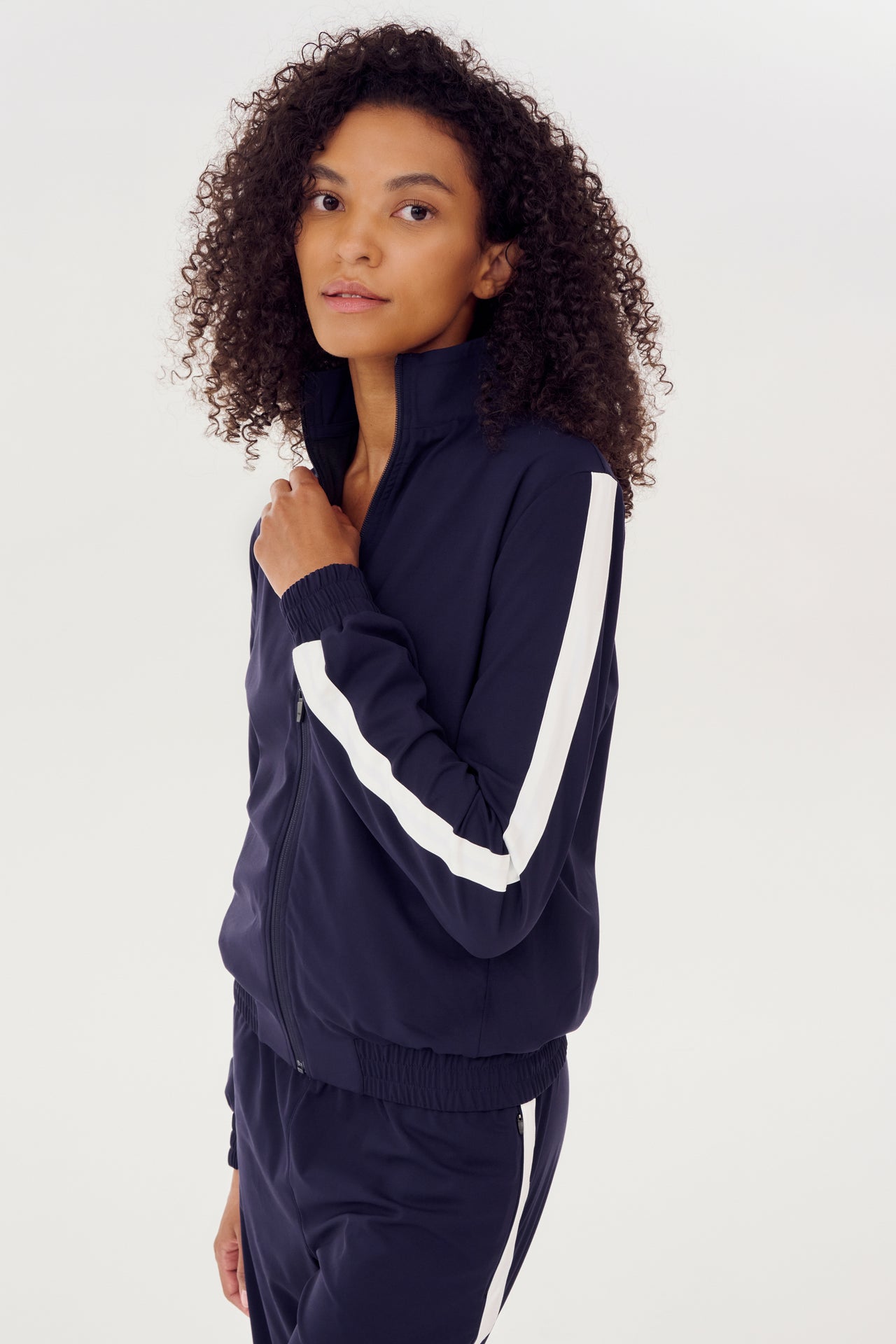A woman wearing a navy Max Rigor Track Jacket and pants made of SPLITS59 fabric, with white side stripes.