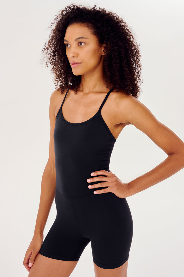 Side view of girl with hand on hip in black high thigh spaghetti strap body suit/one piece 
