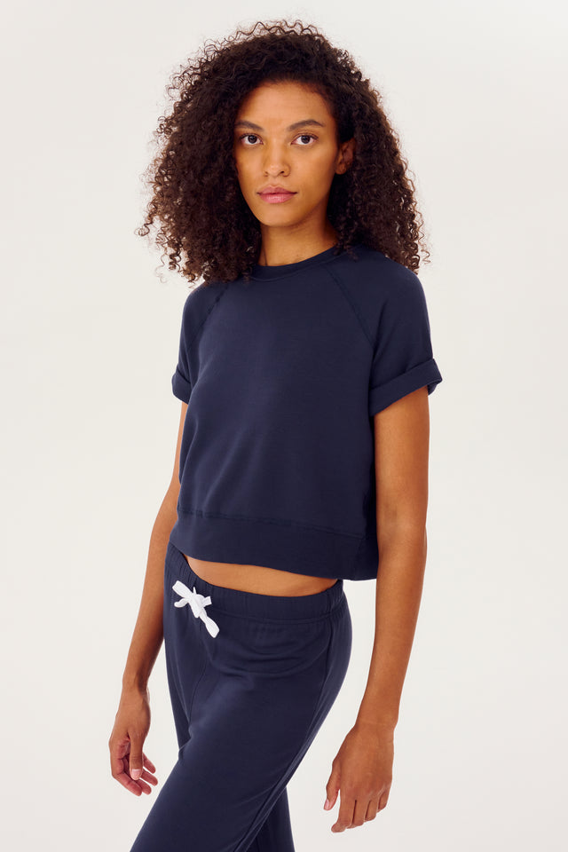 Side view of girl wearing dark blue cropped short sleeve sweatshirt with sweatpants with a white string around waist