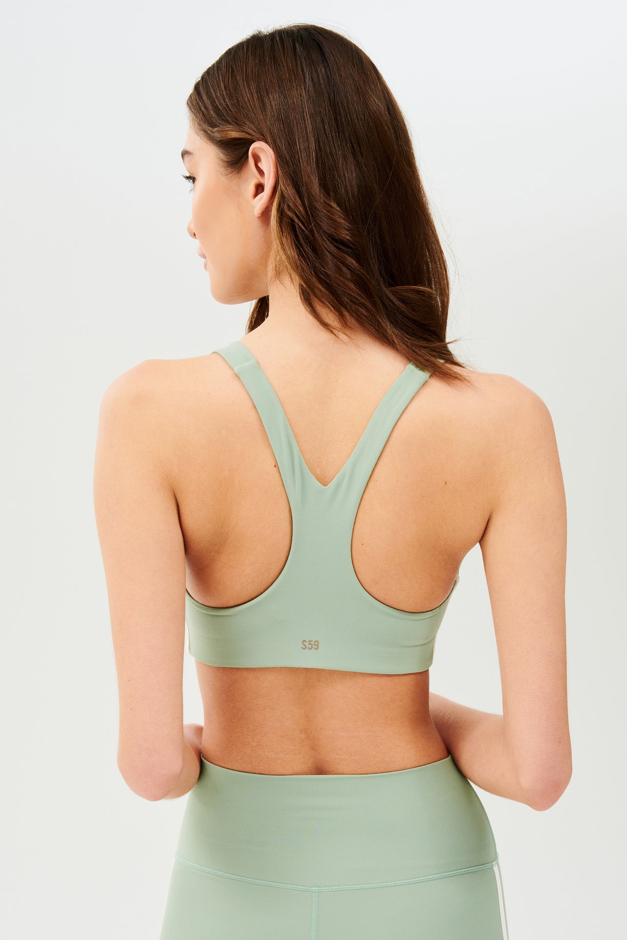 Back view of girl wearing light green sports bra with two thin white stripes down the side and light green leggings 