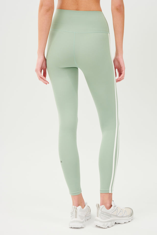 Back view of girl wearing light green leggings with two thin white stripes down the side with white shoes