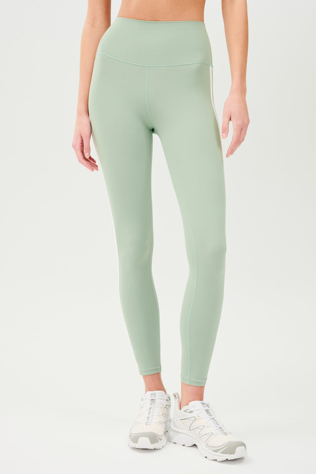 Front view of girl wearing light green leggings with two thin white stripes down the side with white shoes