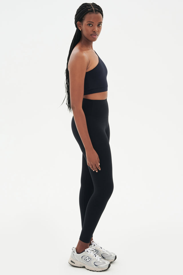 Full side view of girl wearing a black one shoulder bra and a black leggings with grey shoes