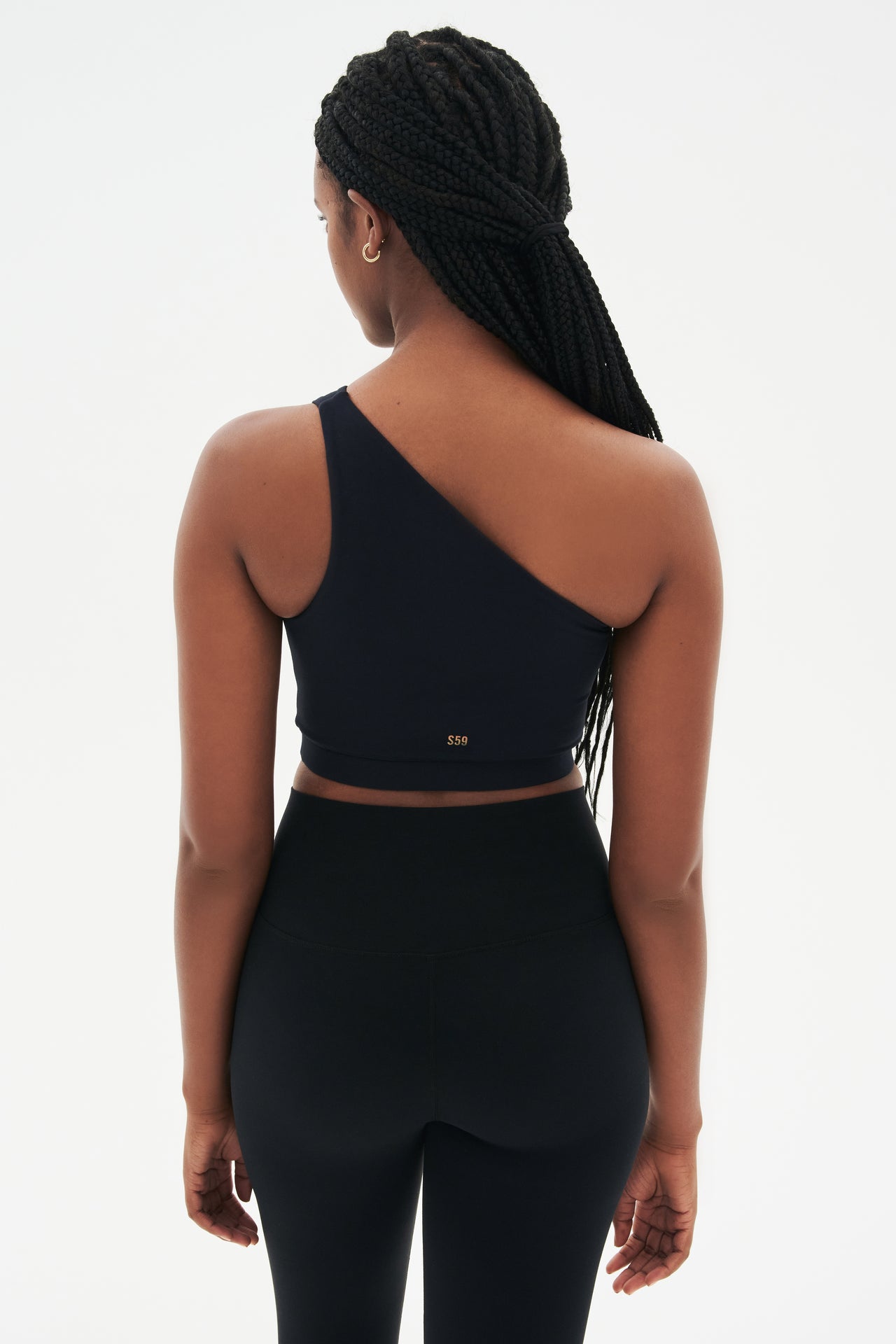 Back view of girl wearing a black one shoulder bra with small logo on the back and a black leggings with grey shoes