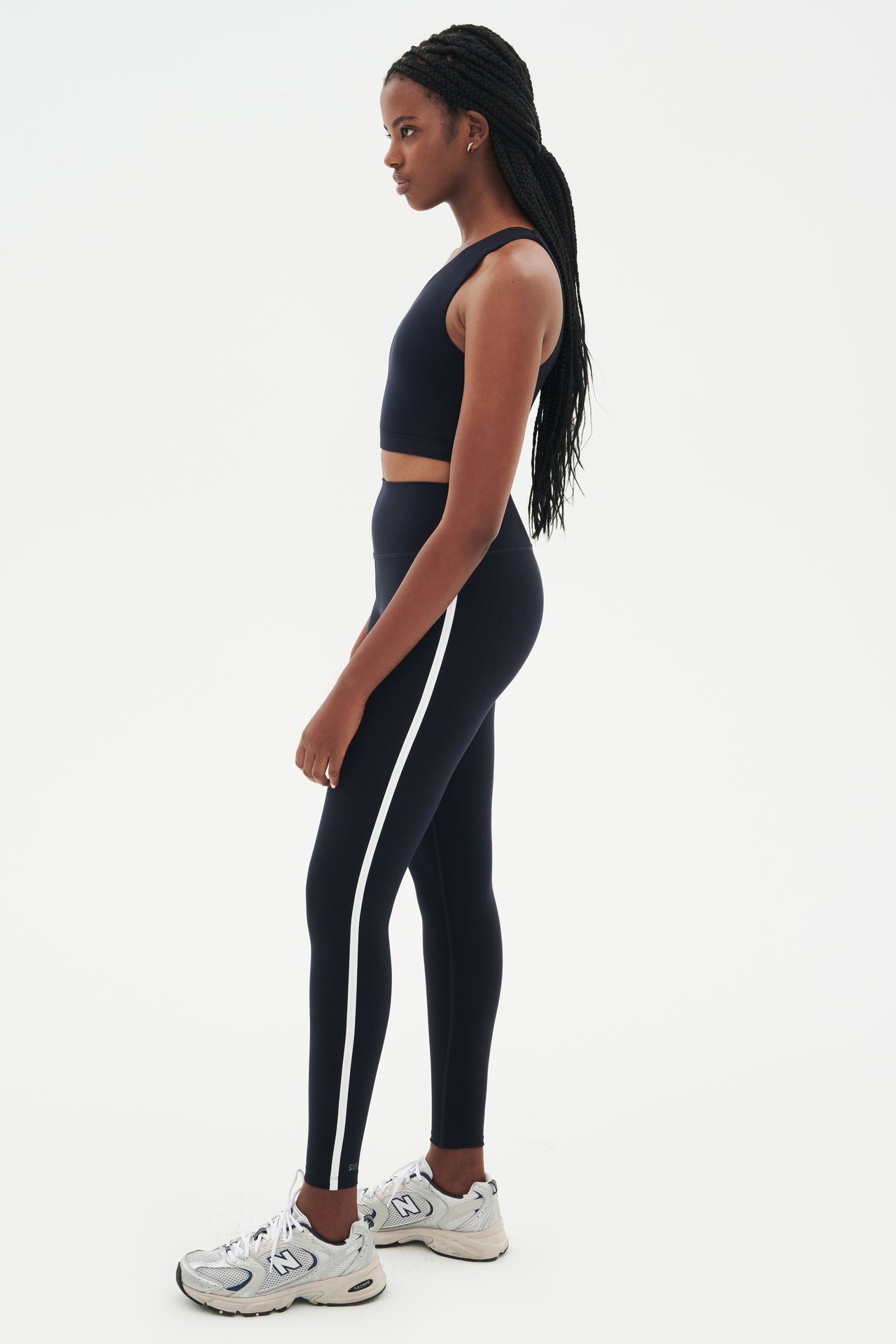 Full side view of girl wearing a dark blue one shoulder bra and a black leggings with a white stripe down the side and with grey shoes