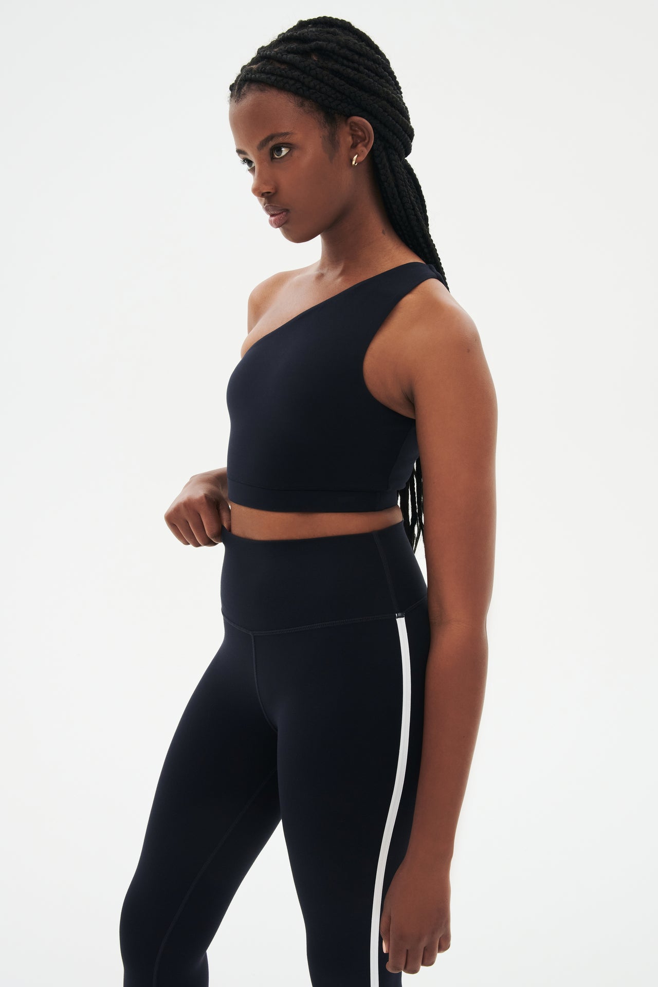 Side view of girl wearing a dark blue one shoulder bra and a black leggings with a white stripe down the side 
