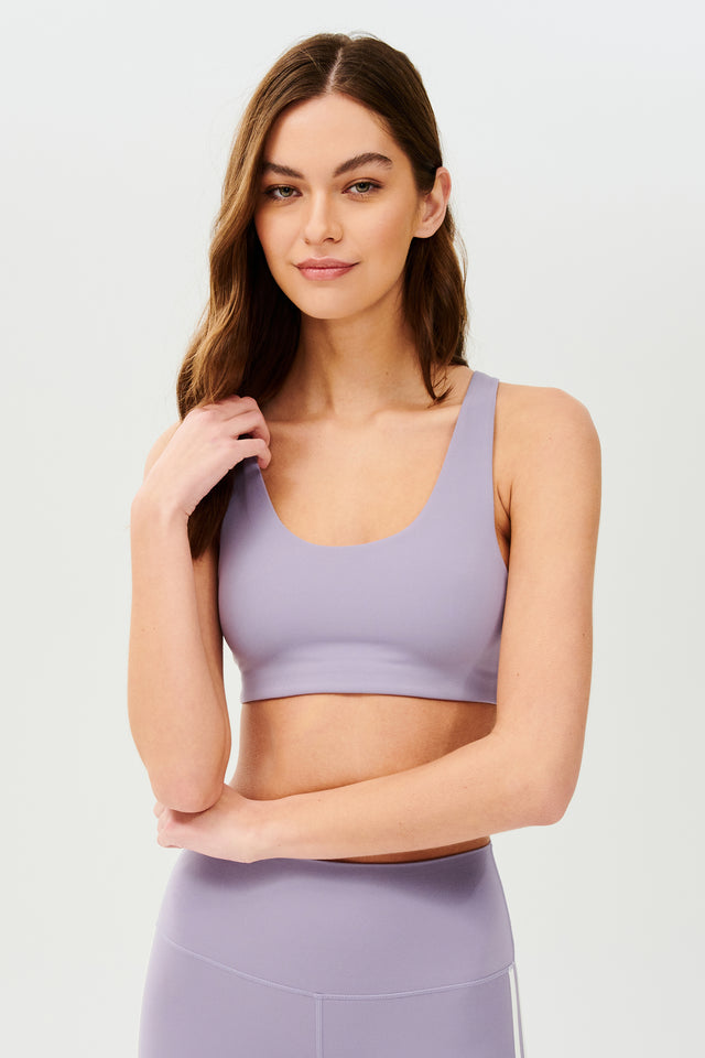 Front view of girl wearing light purple sports bra with two thin white stripes down the side and light purple leggings 