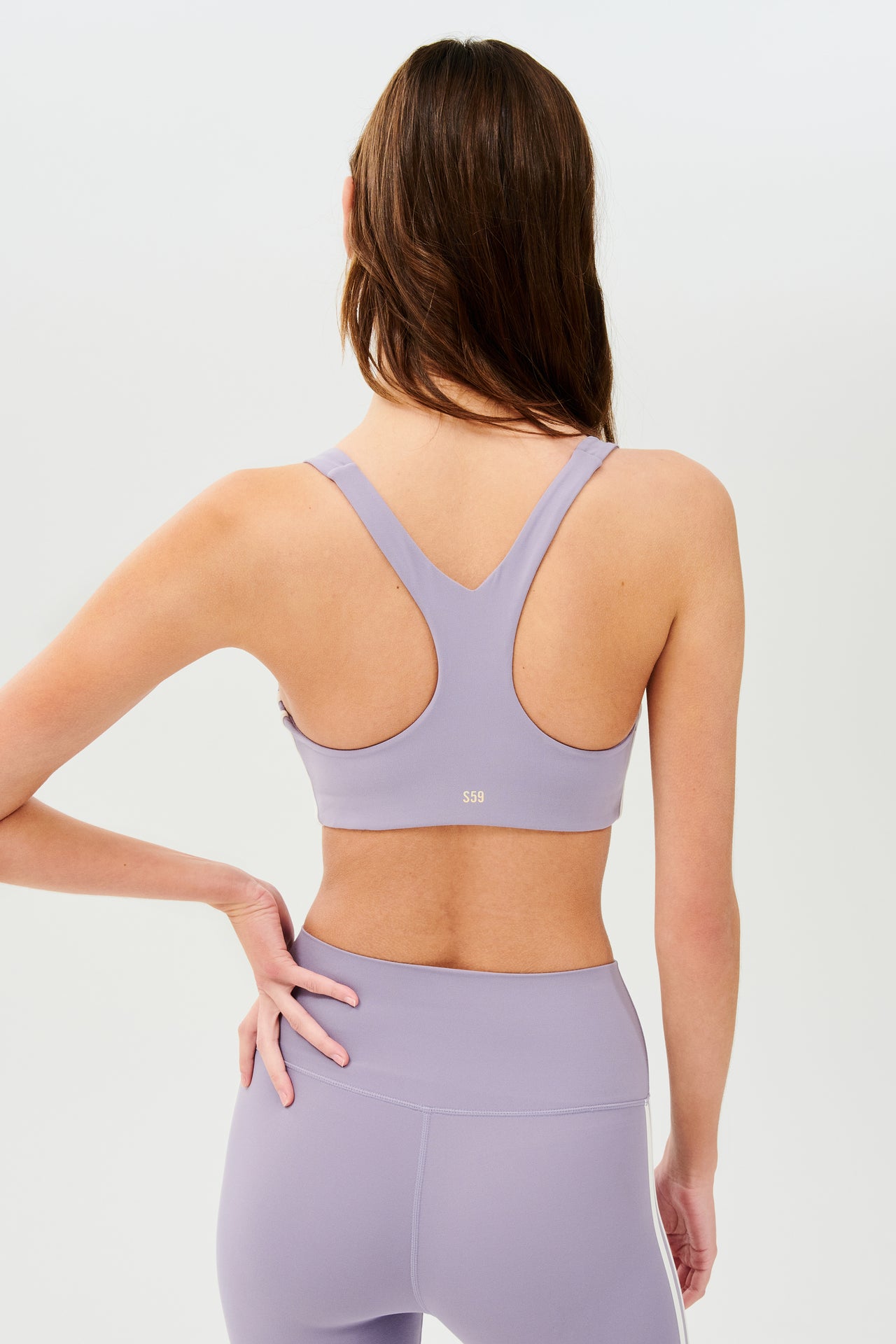 Back view of girl wearing light purple sports bra with two thin white stripes down the side and light purple leggings 