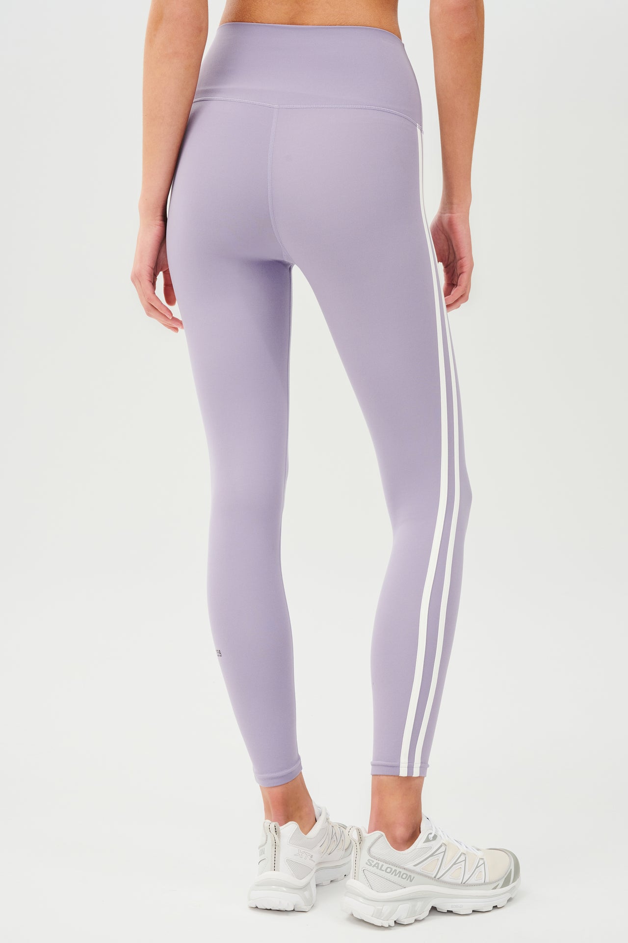 Back view of girl wearing light purple leggings with two thin white stripes down the side with white shoes