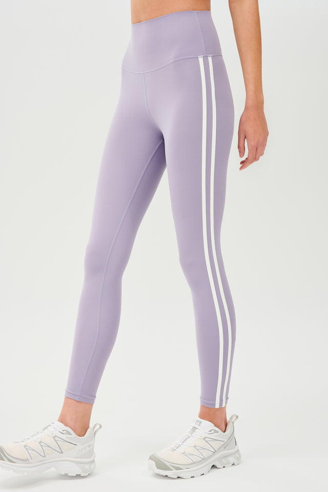 Side view of girl wearing light purple leggings with two thin white stripes down the side with white shoes
