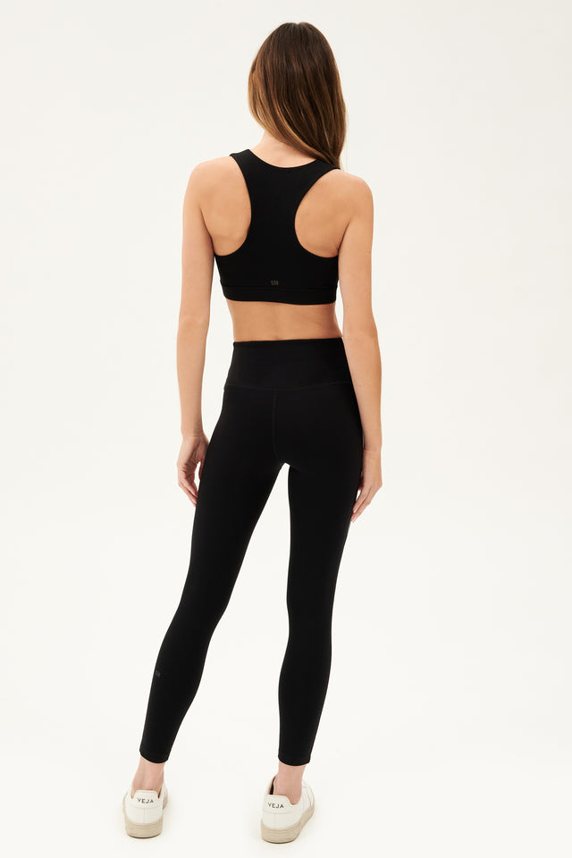 Full back view of girl wearing black square neck sports bra and black leggings with white shoes