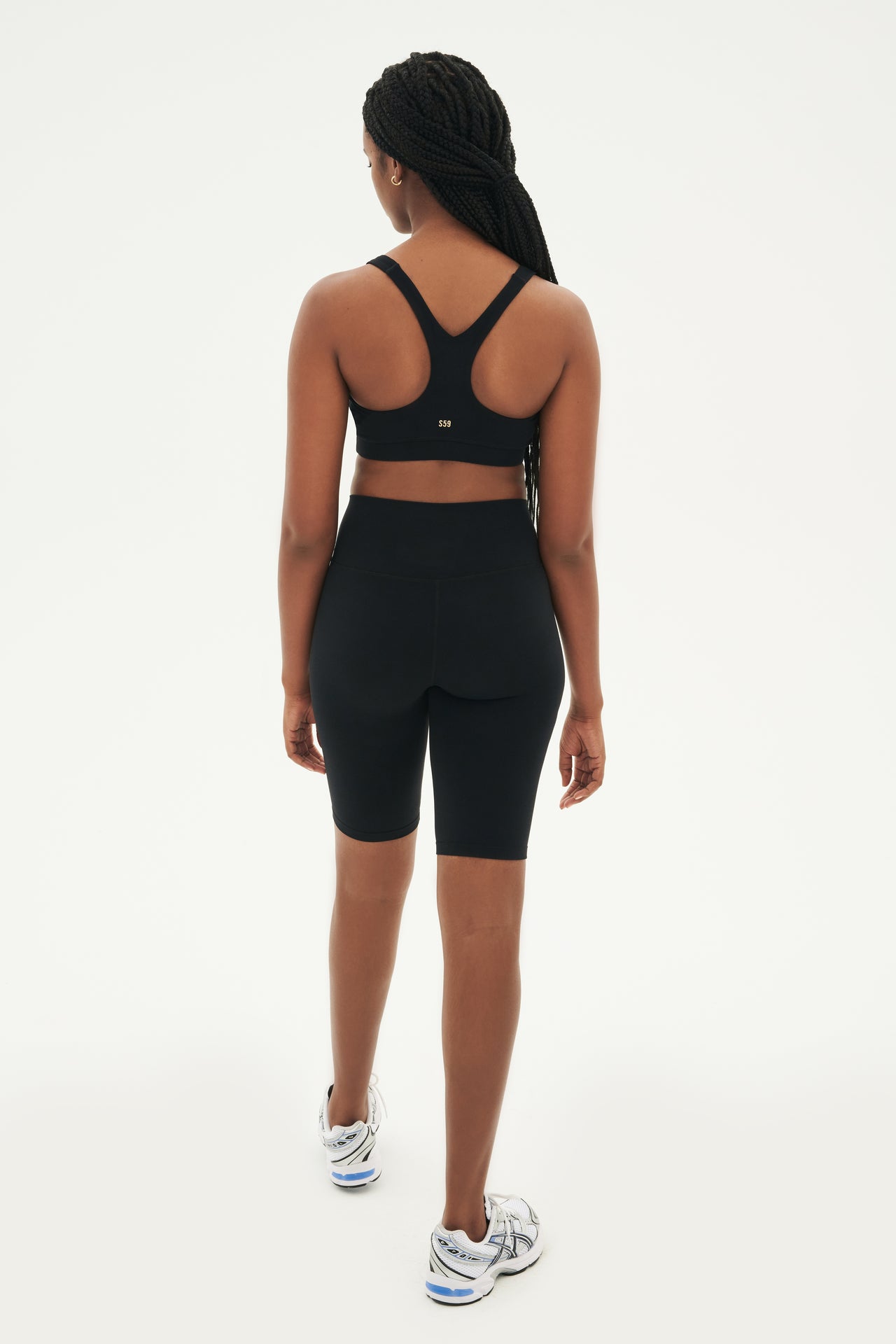 Full back view of girl wearing black sports bra and black high waisted bike shorts that stop right above the knee with white and grey shoes